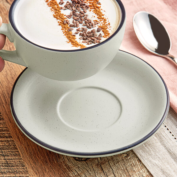 A grey Acopa stoneware saucer with a cup of coffee and a spoon on a table.