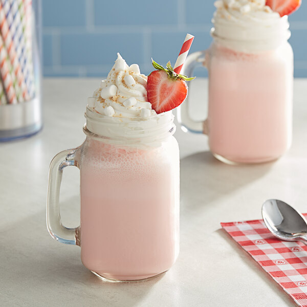 A glass mug filled with a pink milkshake topped with whipped cream and a strawberry.