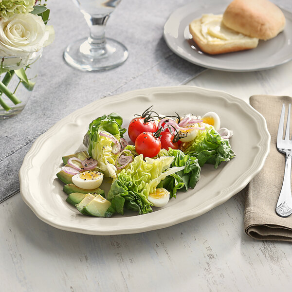 A white porcelain platter with a scalloped edge holding a plate of salad and a fork.