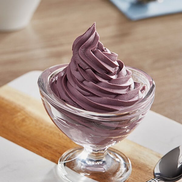 A glass bowl of purple ice cream with a spoon in it.