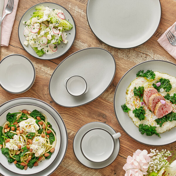 A gray matte stoneware cup with a handle, shown on a matching saucer among various plates of food.