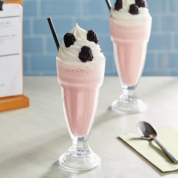 Two glasses of pink milkshakes made with Oringer Black Raspberry Milkshake Base Syrup and topped with blackberries and whipped cream.