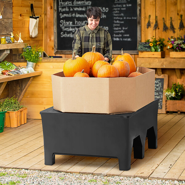 A man standing next to a MasonWays plastic bulk produce merchandiser full of pumpkins on a table in an organic food store.