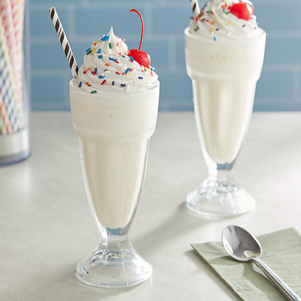 A glass of Oringer milkshake with whipped cream and sprinkles on a table.