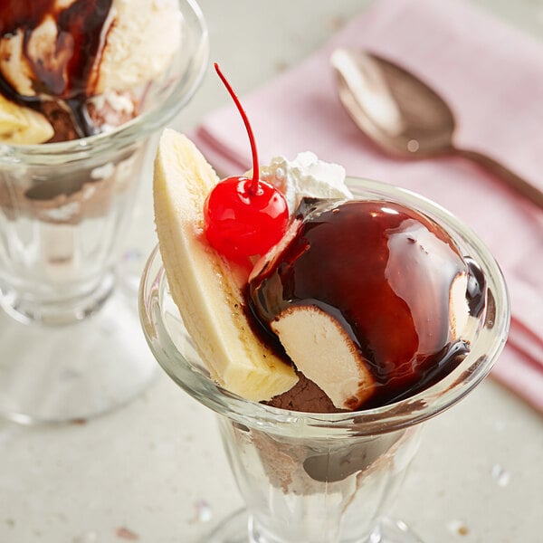 A dessert in a glass with Oringer Deluxe Hot Milk Fudge Topping, chocolate, and vanilla ice cream, and a cherry.