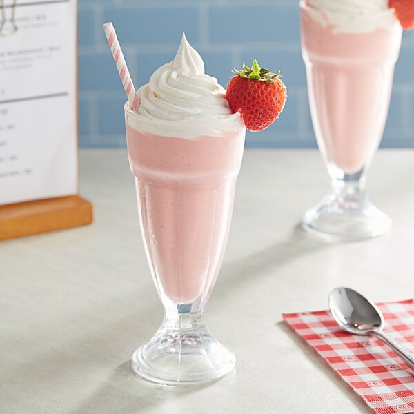 A glass of pink milkshake with a straw and a strawberry on top.
