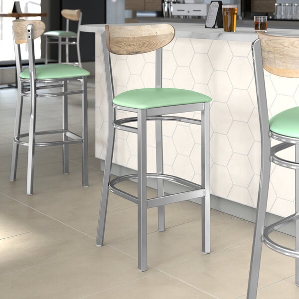 Lancaster Table & Seating Boomerang bar stools with Seafoam Vinyl seats and Driftwood backs on a counter in a restaurant.