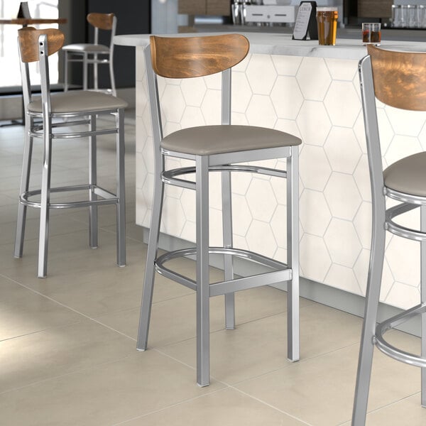 Lancaster Table & Seating bar stools with dark gray vinyl seats and vintage wood backs at a restaurant counter.