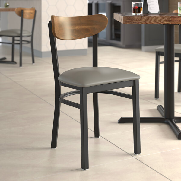 A Lancaster Table & Seating Boomerang chair with dark gray vinyl seat and wood back at a restaurant table.