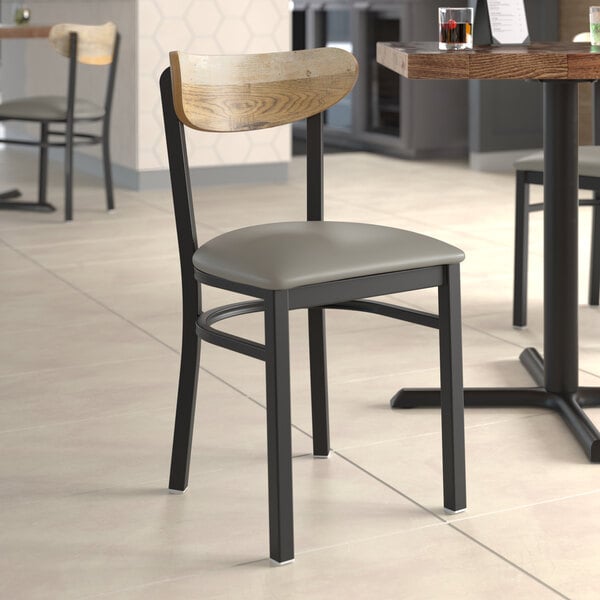 A Lancaster Table & Seating Boomerang Series chair with a dark gray vinyl cushion next to a table in a restaurant.