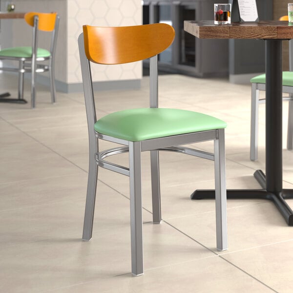 A Lancaster Table & Seating Boomerang chair with a seafoam vinyl seat and cherry wood back on a table in a restaurant.