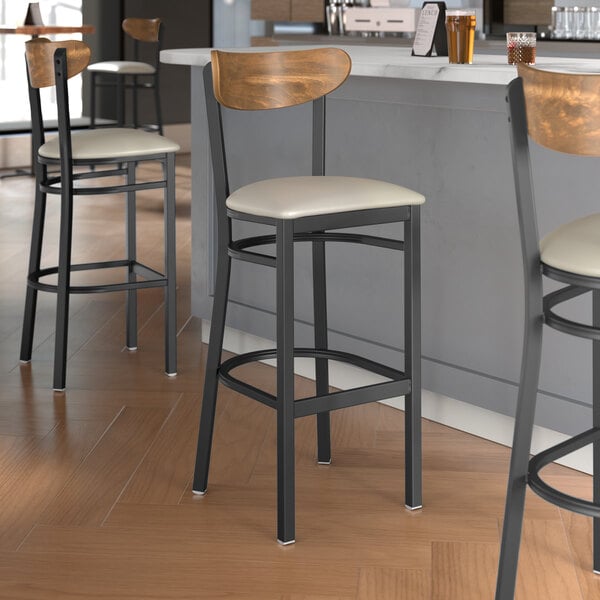 Lancaster Table & Seating bar stools with light gray vinyl seats and vintage wood backs on a black metal frame.