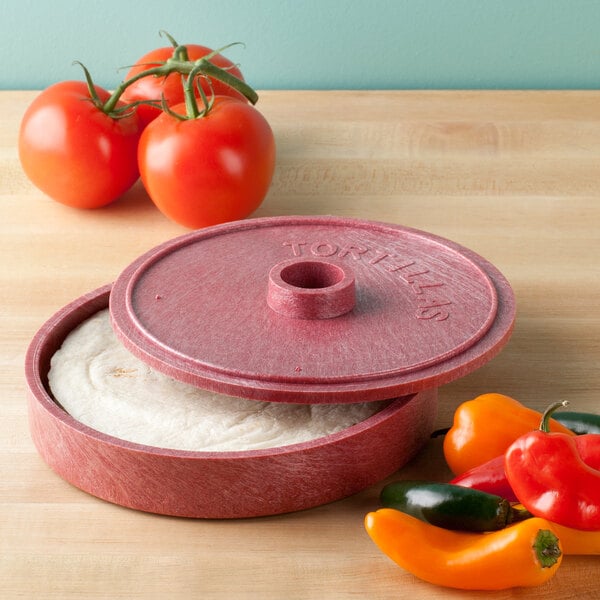 A red circular HS Inc. polyethylene tortilla server with food inside on a table next to tomatoes.
