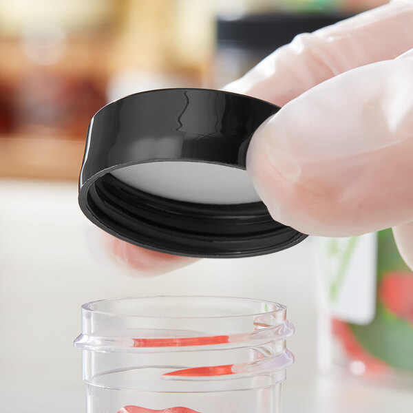 A person in gloves holding a black plastic cap over a plastic container.