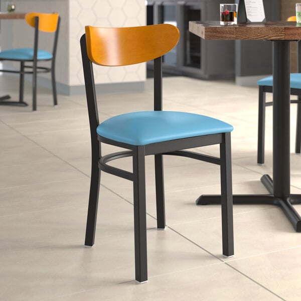 A Lancaster Table & Seating Boomerang Series chair with a blue vinyl seat and cherry wood back at a restaurant table.