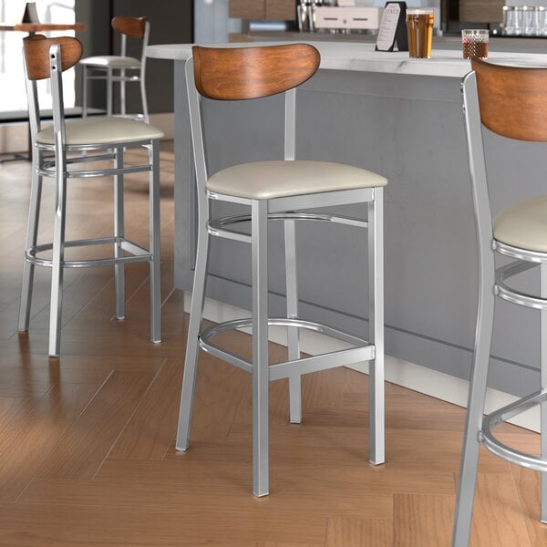 Lancaster Table & Seating Boomerang Series bar stools with light gray seats and wood backs.