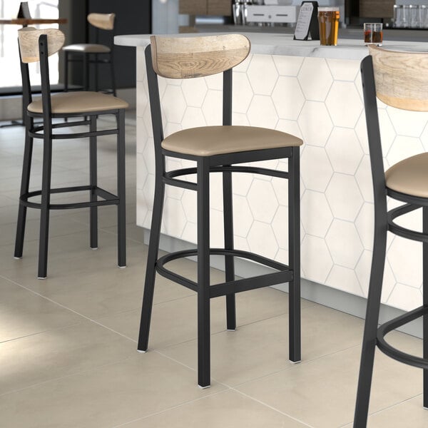 Three Lancaster Table & Seating Boomerang Series bar stools with taupe vinyl seats and driftwood backs on a counter.