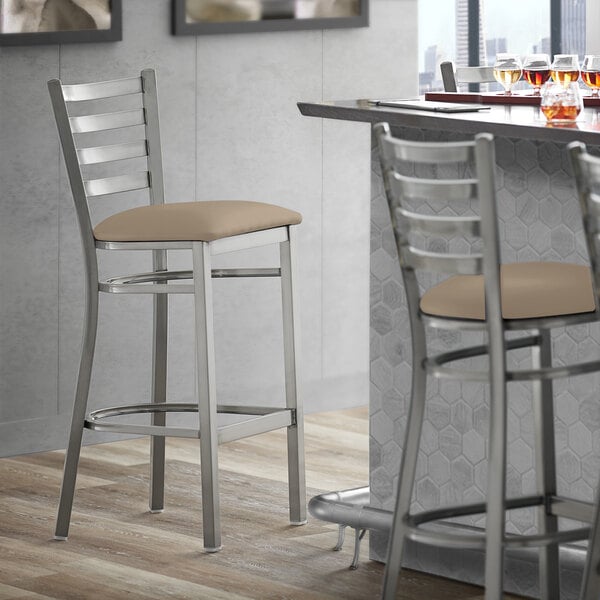A Lancaster Table & Seating ladder back bar stool with taupe vinyl padding.