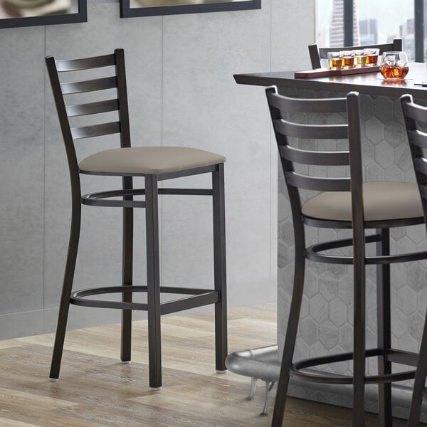 A Lancaster Table & Seating distressed copper ladder back bar stool with a dark gray vinyl padded seat.