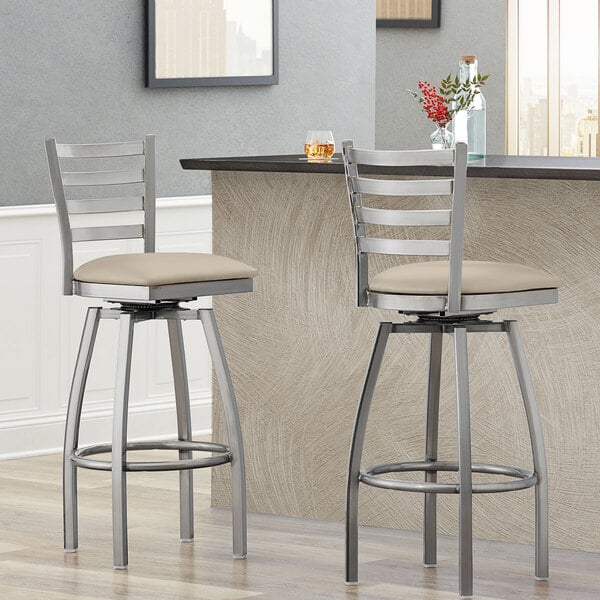 Two Lancaster Table & Seating swivel bar stools with light gray vinyl padded seats at a counter.