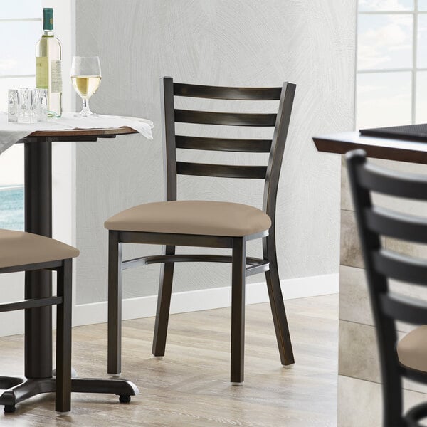 A Lancaster Table & Seating ladder back chair with a taupe vinyl padded seat in a restaurant dining area.