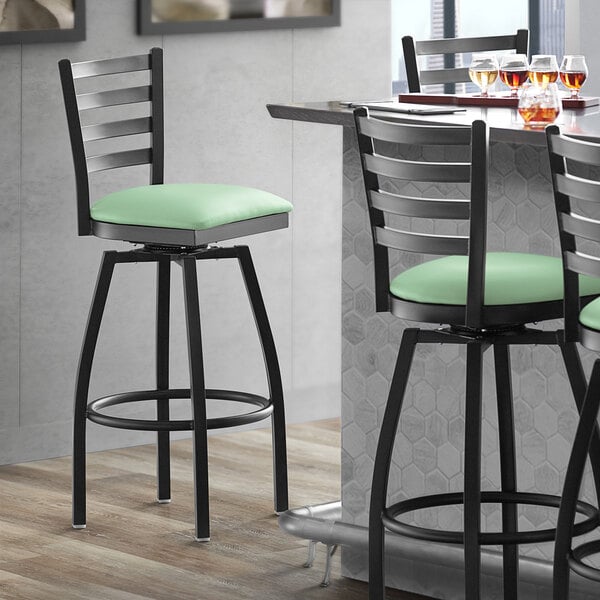 A Lancaster Table & Seating black ladder back swivel bar stool with a seafoam vinyl padded seat.