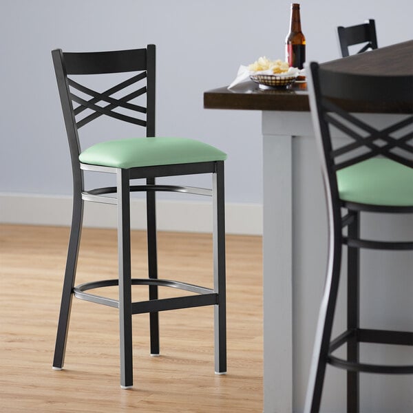 A Lancaster Table & Seating black cross back bar stool with a seafoam green vinyl cushion.