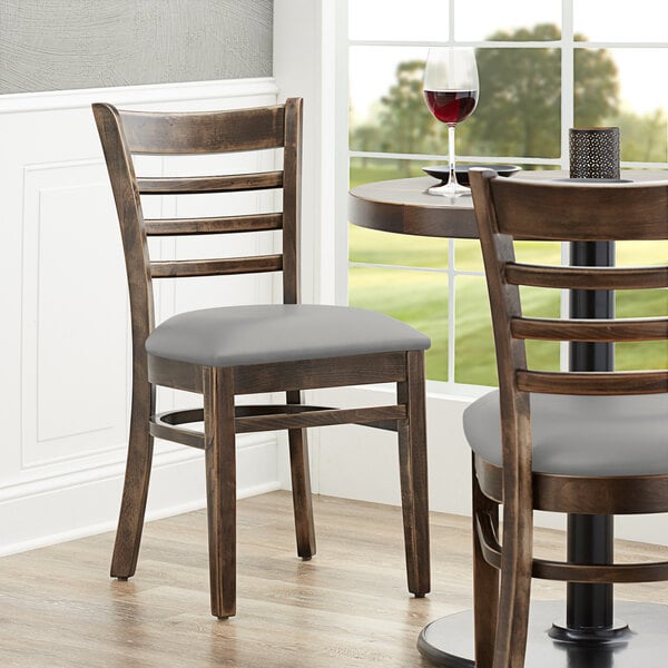 A pair of Lancaster Table & Seating wood chairs with light gray vinyl seats at a table in a restaurant.