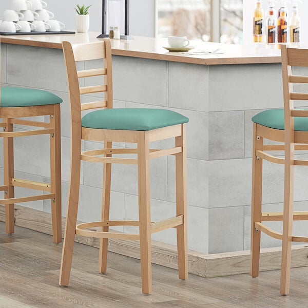 Three Lancaster Table & Seating wood ladder back bar stools with seafoam vinyl seats at a counter.