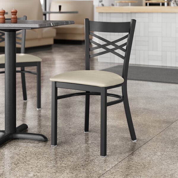 A Lancaster Table & Seating black cross back chair with a light gray vinyl padded seat at a table in a restaurant.