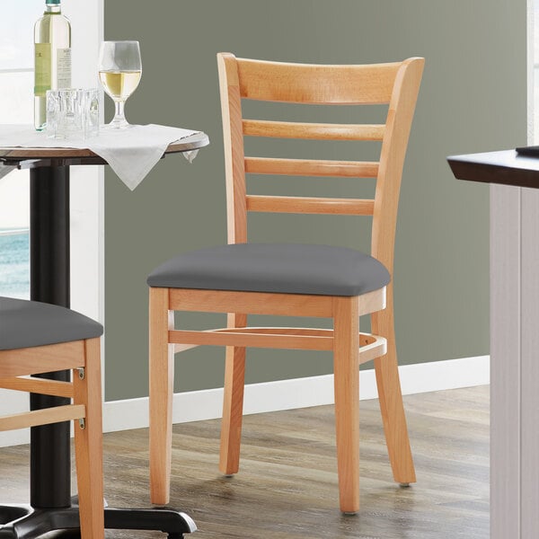 A pair of Lancaster Table & Seating natural finish wood chairs with dark gray vinyl seats on a table in a restaurant.
