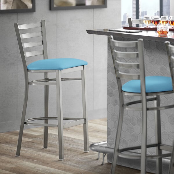 A Lancaster Table & Seating ladder back bar stool with blue vinyl cushion on a counter.