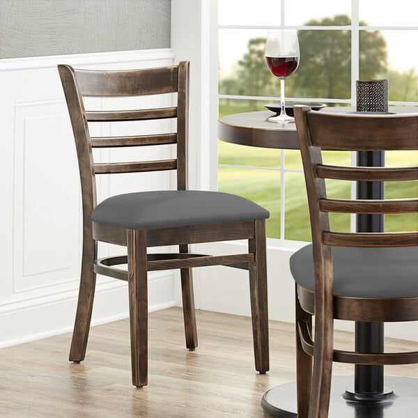 A Lancaster Table & Seating wood chair with a dark gray cushion at a table in a restaurant.