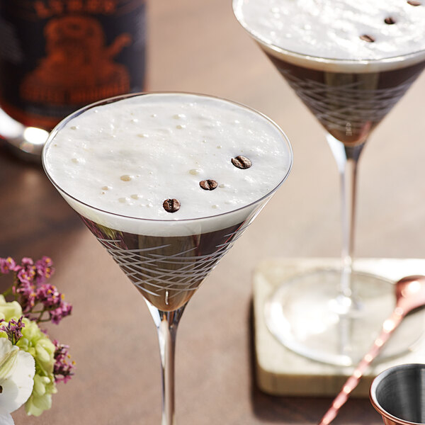Two martini glasses filled with Lyre's Coffee Originale and coffee beans on a table.