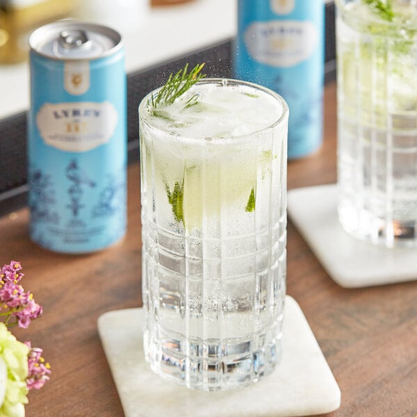 A glass of Lyre's gin and tonic with ice and a lime slice next to a blue Lyre's can.