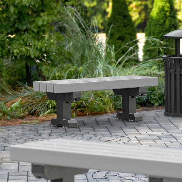A MasonWays gray plastic backless Dura-Bench with black legs next to a trash can on a brick patio.