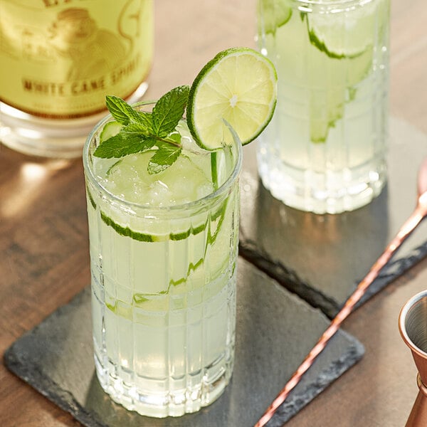 A glass of Lyre's White Cane Spirit with lime slices and mint leaves.