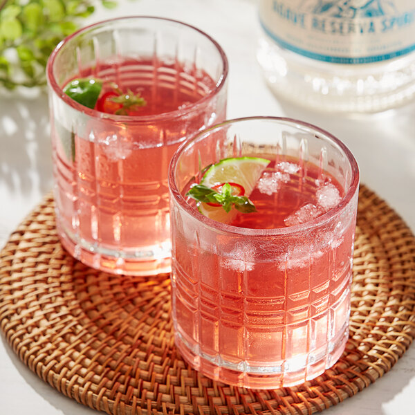 A Lyre's Agave Reserva non-alcoholic tequila bottle and two glasses of pink liquid with lime and mint.