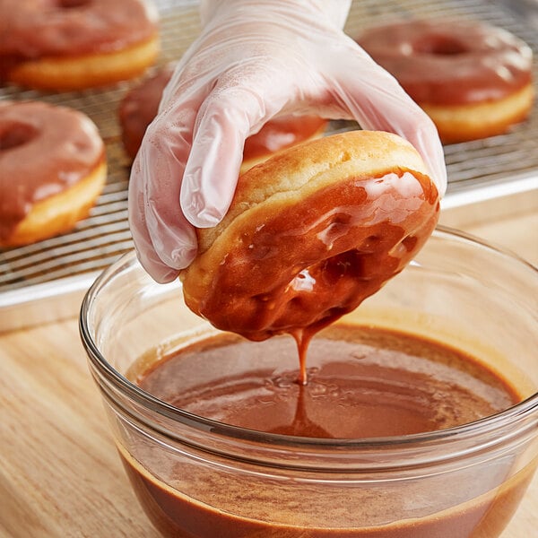 A hand holding a glazed donut over a bowl of Rich's Allen Classic Caramel Icing.