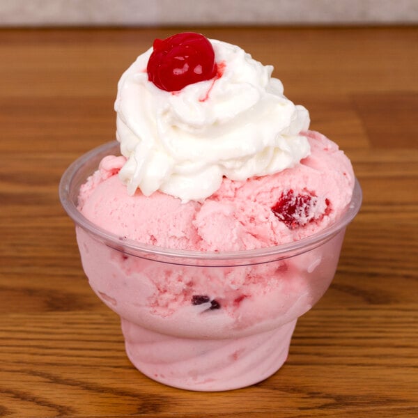 A clear Fabri-Kal PET sundae cup filled with ice cream topped with whipped cream and a cherry.