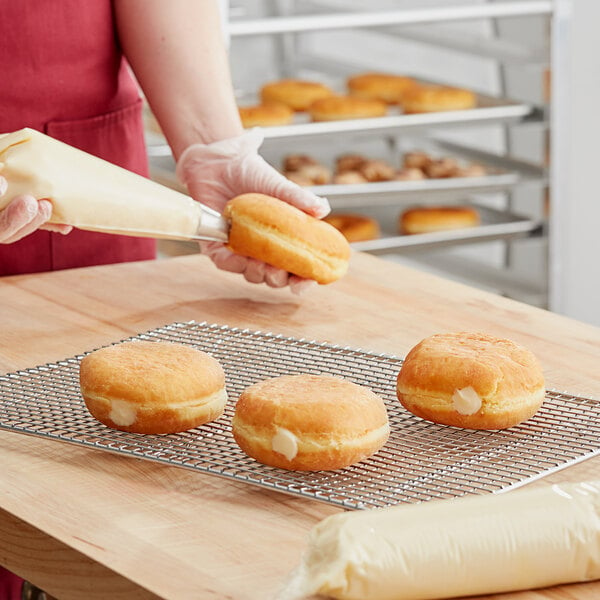 A person using Rich's Allen Cream Cheese Filling in a pastry bag to fill a doughnut.