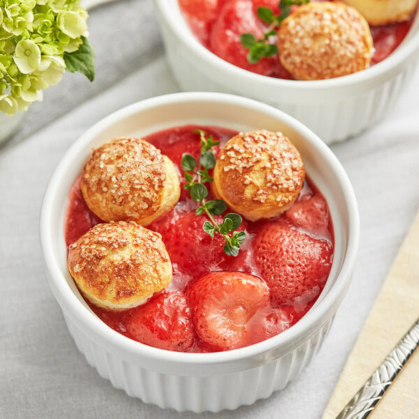 Two bowls of Dole whole strawberries with small round objects on a table.