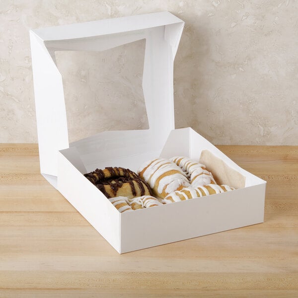 A white auto-popup bakery box filled with pastries with icing and chocolate.