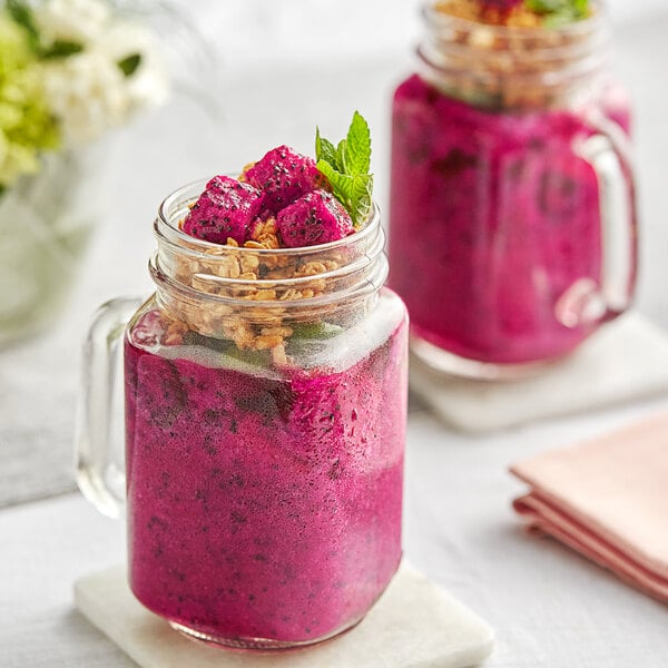 A glass jar with a pink smoothie made with Dole Pitaya chunks and topped with granola and fruit.