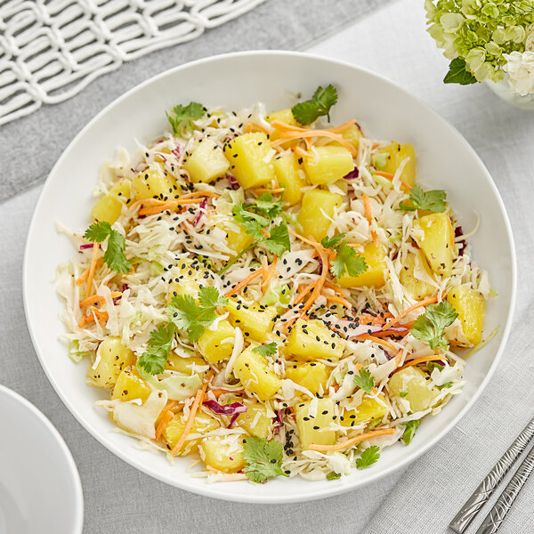 A bowl of pineapple salad with carrots and sesame seeds on a table.