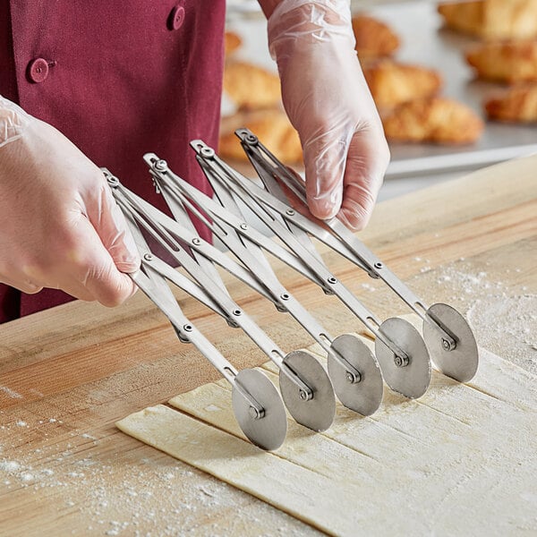 A person holding a stainless steel pastry cutter with 5 wheels.