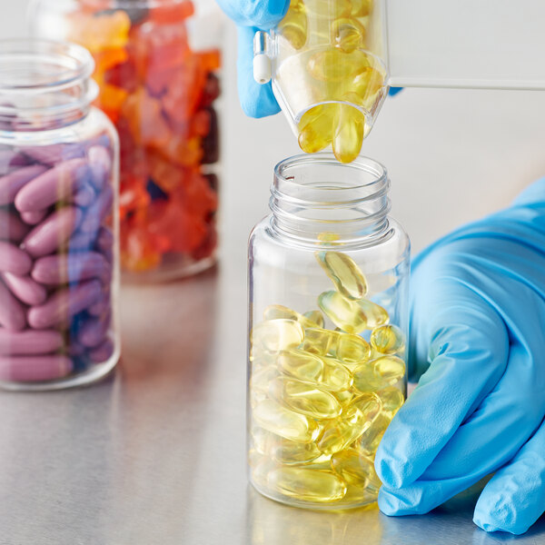 A hand in blue gloves pouring yellow pills into a clear 150cc packer bottle.