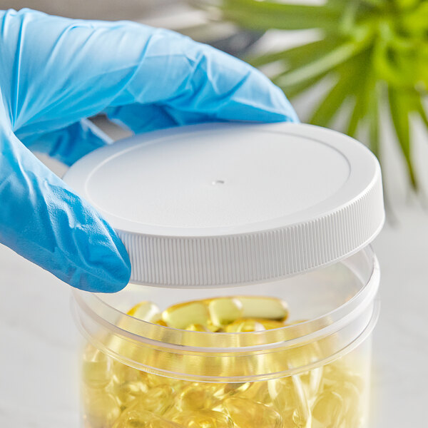 A hand in a blue glove holding a 89/400 white plastic lid over a container of yellow pills.