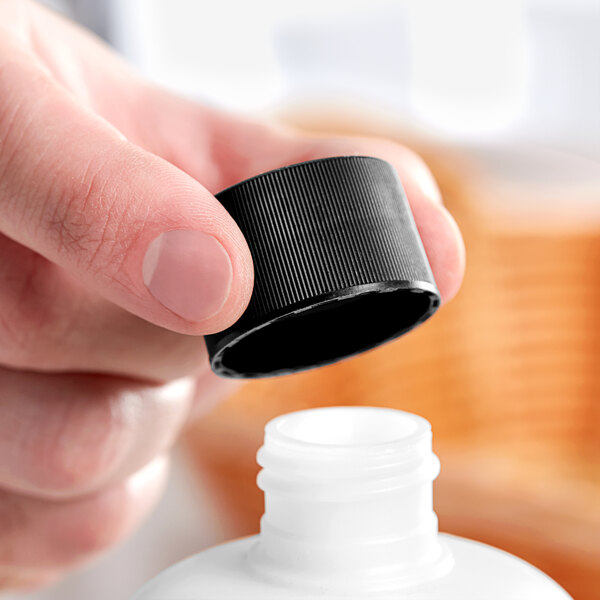 A hand holding a 28/410 black continuous thread lid over a white plastic bottle