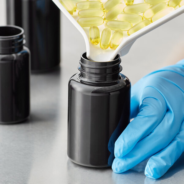 A gloved hand pours yellow pills into a dark amber 175cc packer bottle.